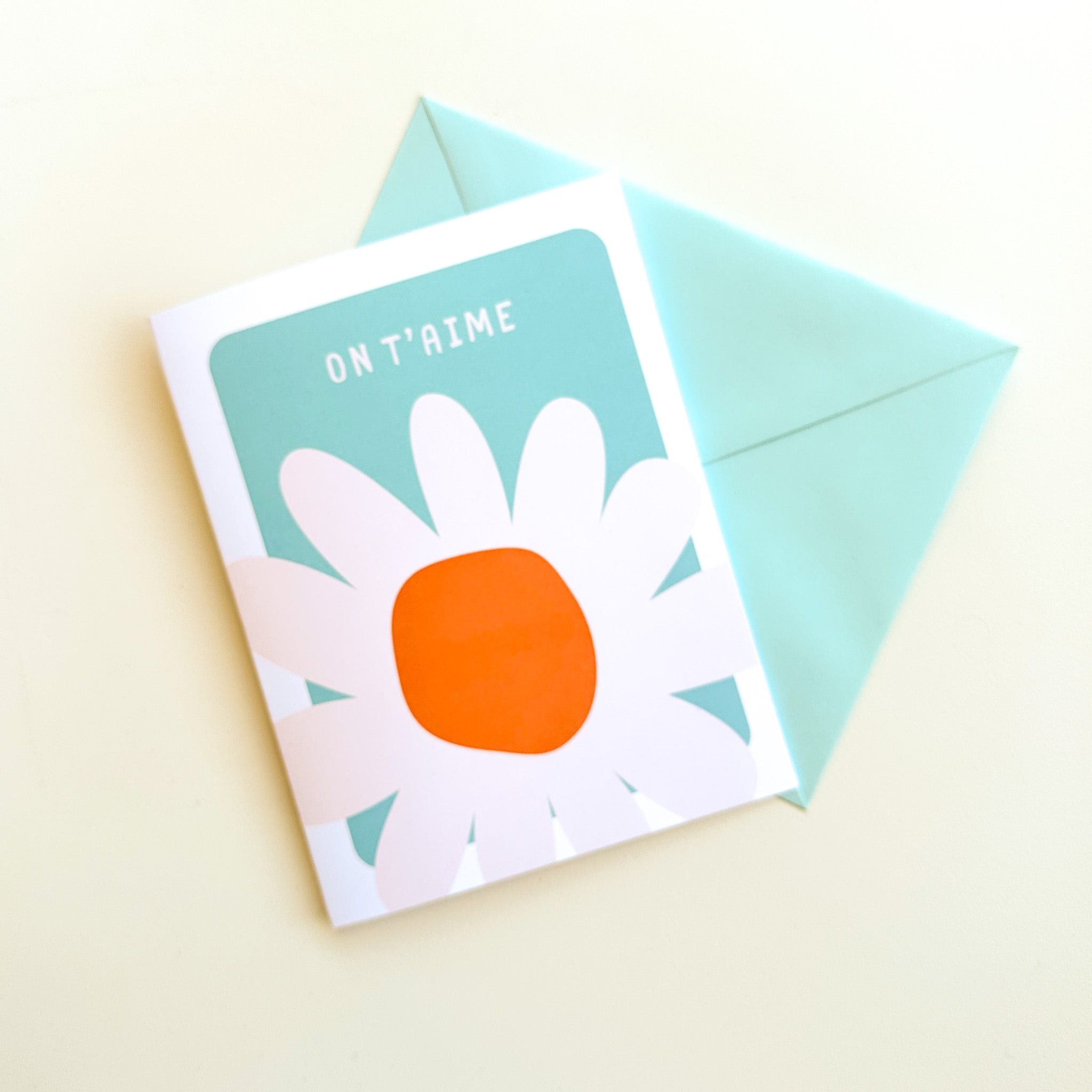Carte de voeux Illustration minimaliste d'une marguerite blanche avec typographie moderne affichant On t'aime sur fond pâle